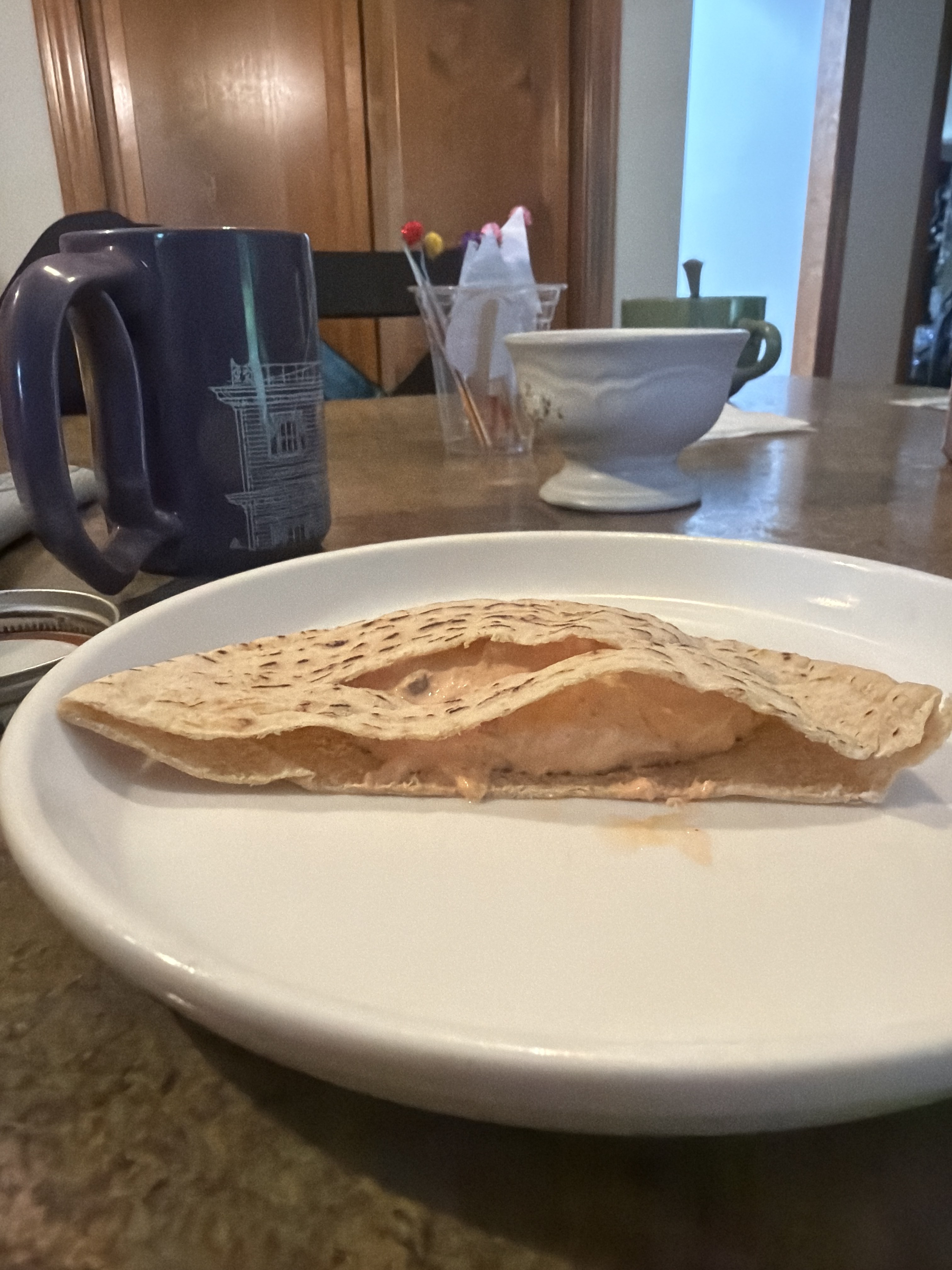 A pita pocket stuffed with tuna salad on a white plate, a blue mug in the background